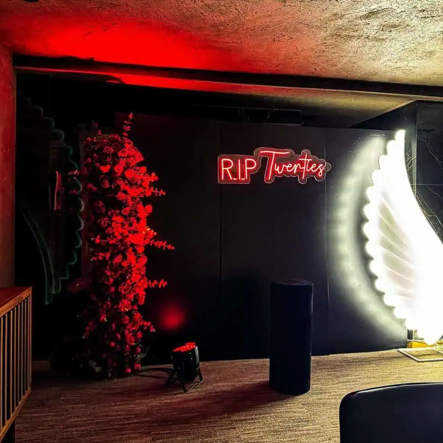 RIP twenties-themed 30th birthday backdrop with neon lights and dramatic red decor.