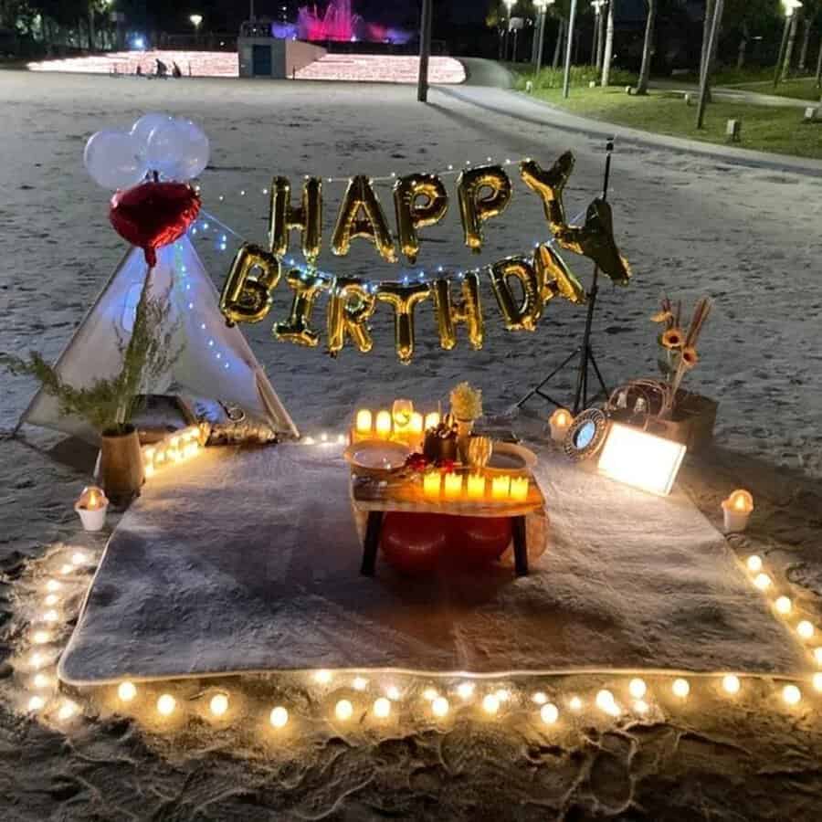 Beachside 30th birthday setup with lights, candles, and "Happy Birthday" balloon decor.