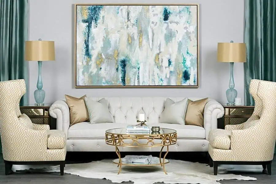 Teal living room with tufted white sofa, abstract wall art, gold accents, and patterned chairs.