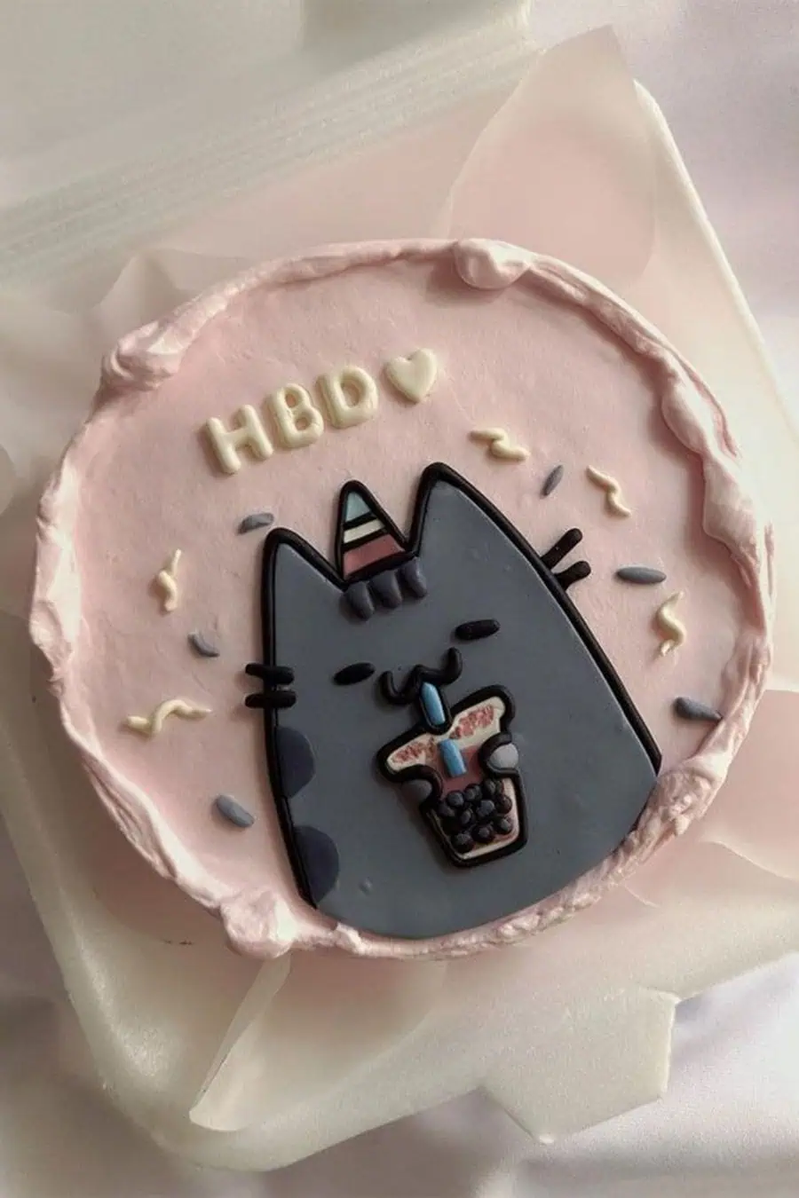 Cute pink birthday cake with a cartoon cat design and "HBD" decoration.