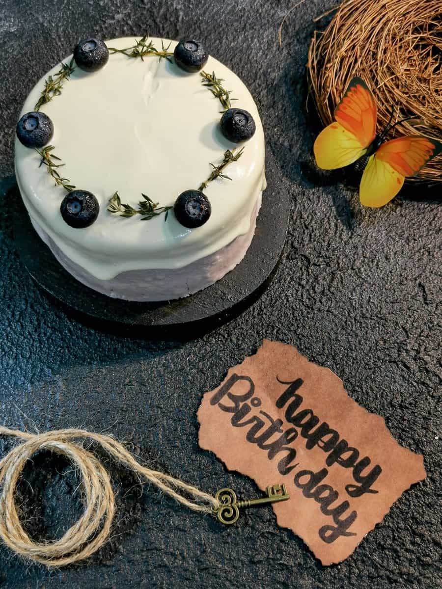 Minimalist birthday cake decorated with blueberries and thyme, accompanied by a "Happy Birthday" note.