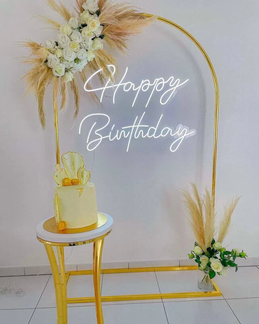 Minimalist birthday party with gold accents, pampas grass, white roses, and a neon "Happy Birthday" sign.