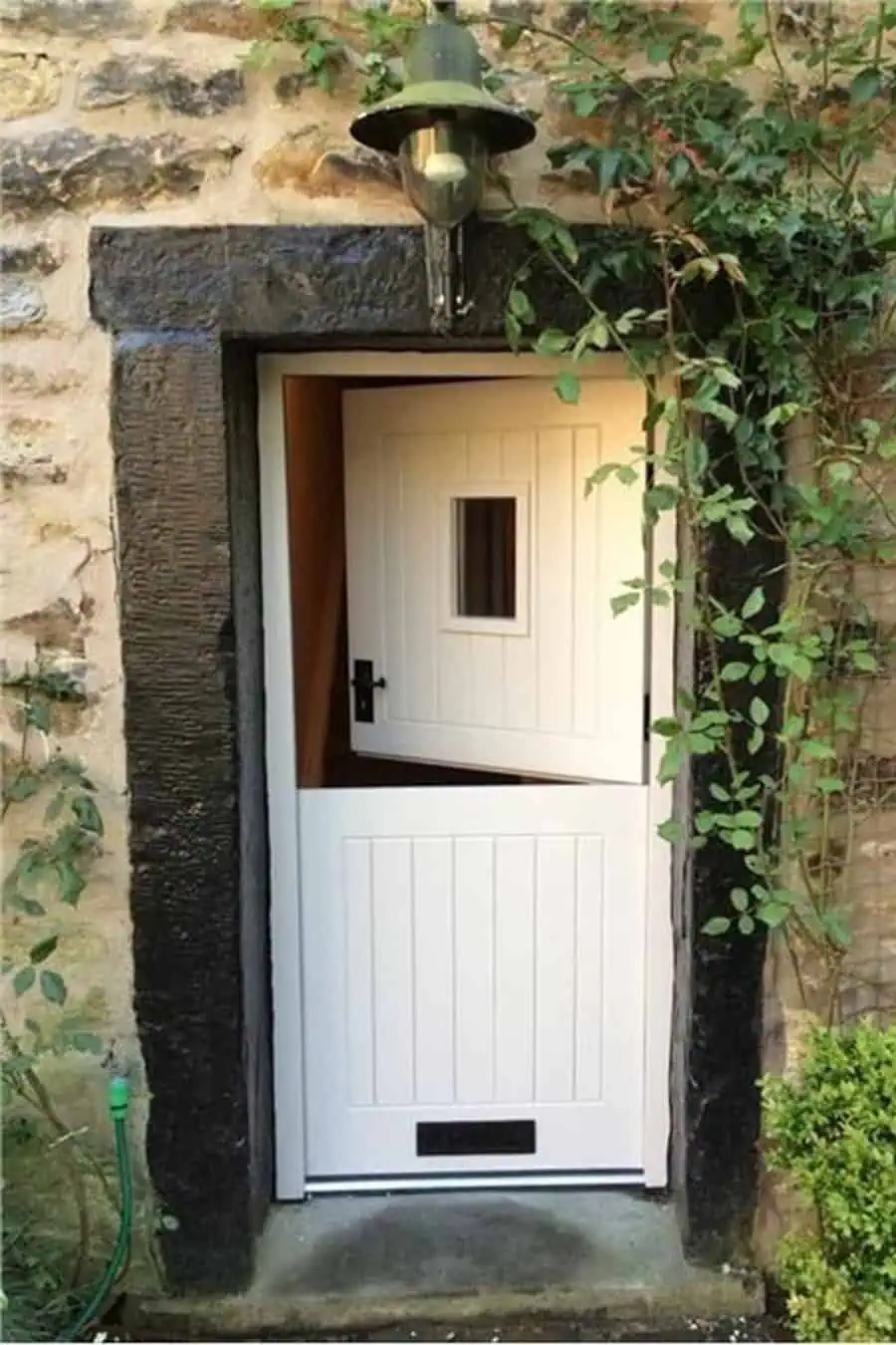 White Dutch door with vertical panels, a small window, and rustic stone wall with greenery.