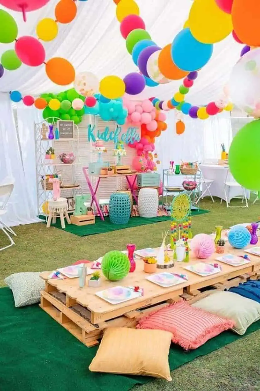 Colorful balloon-themed outdoor birthday party setup with low seating and vibrant table decor.