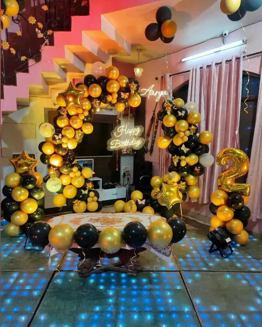 Surprise birthday party with black and gold balloons, neon sign, and number 2 decoration.