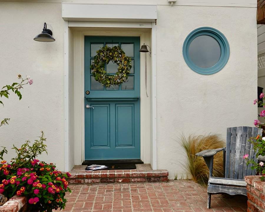Teal Dutch door with a floral wreath, brick steps, and vibrant flowers in a cozy bungalow entryway.