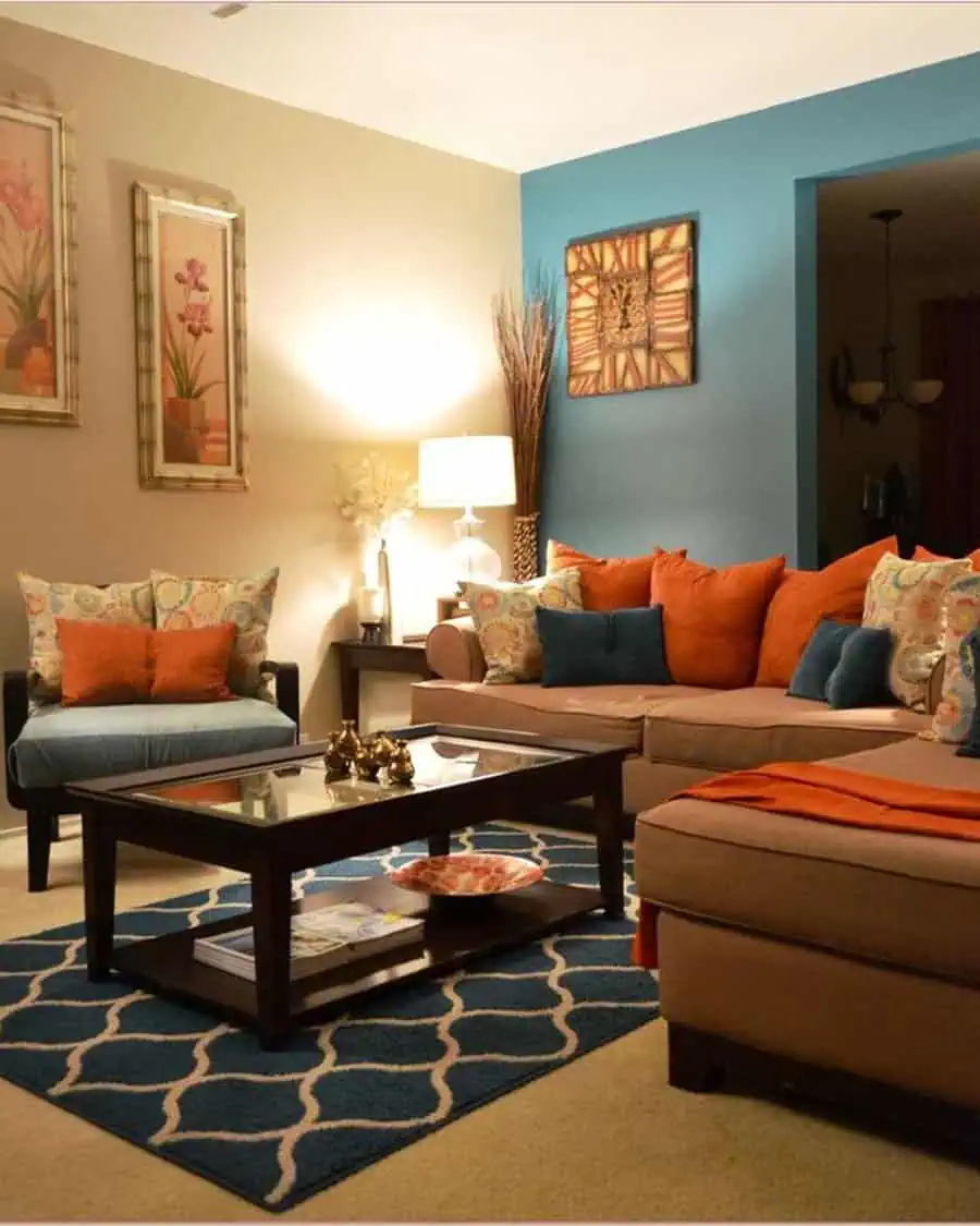 Warm living room with teal accent wall, burnt orange pillows, beige furniture, and a patterned rug.