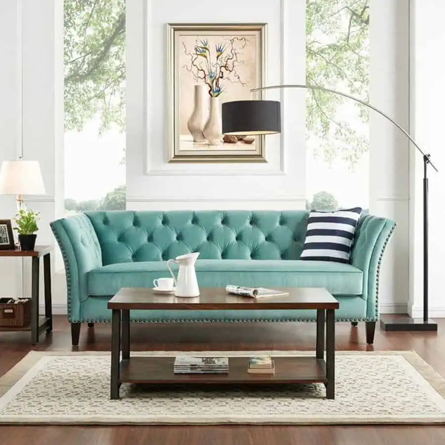 Teal tufted Chesterfield sofa with striped cushion and wooden coffee table in a bright living room.