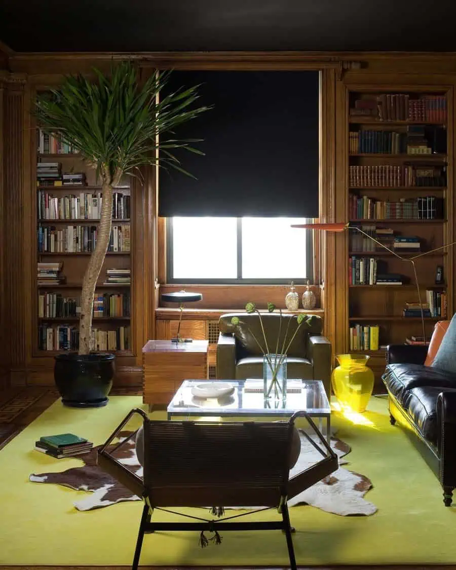 Classic den with wooden bookshelves, leather seating, vibrant rug, and a tall indoor plant.