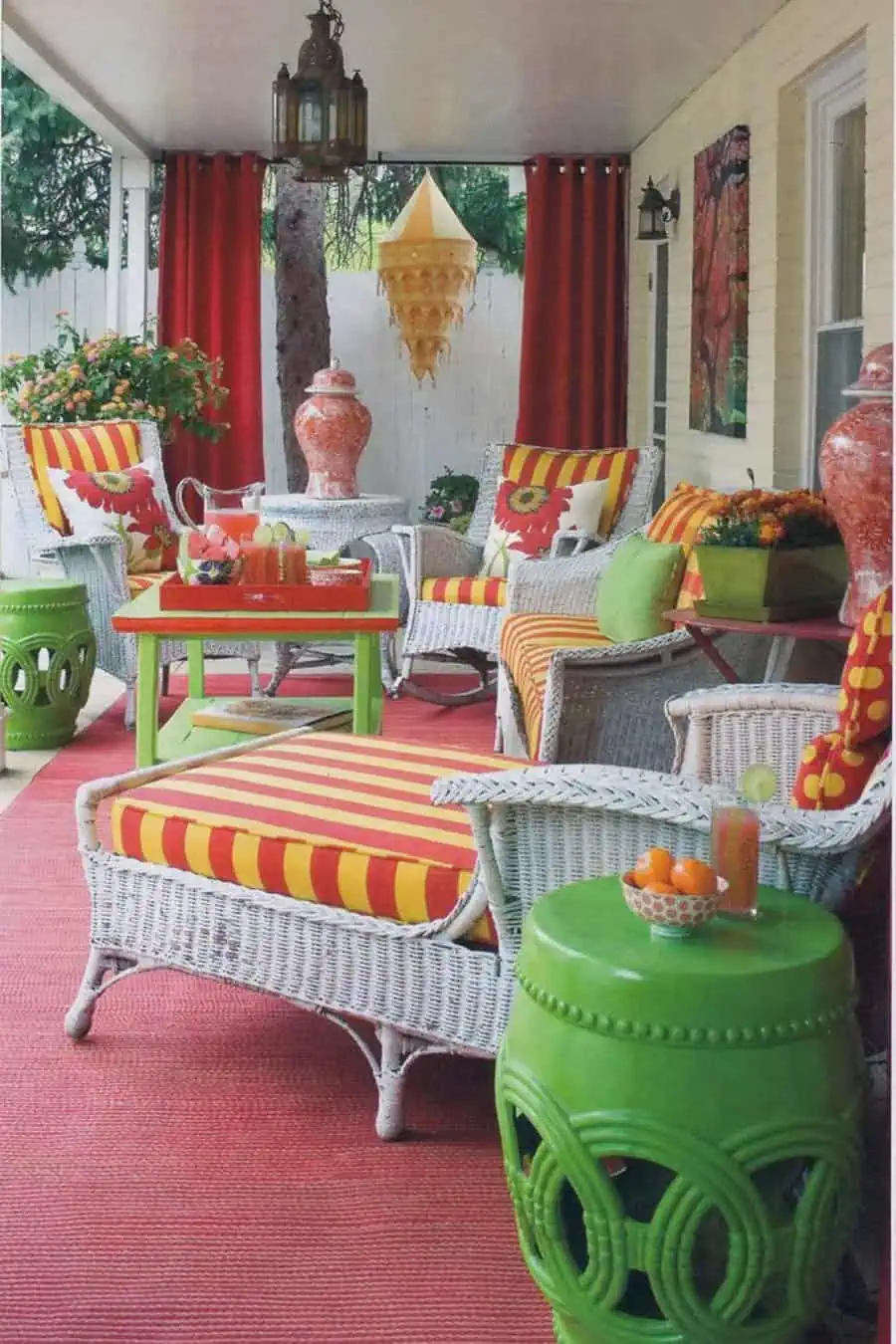 Eclectic patio with white wicker furniture, bold striped cushions, red curtains, and green accents.