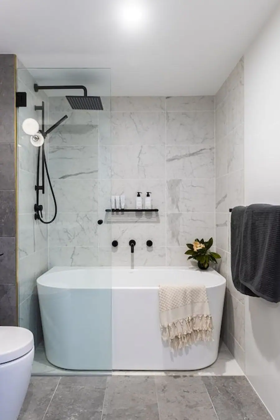 Small luxury bathroom with freestanding bathtub, marble walls, black fixtures, and modern decor.