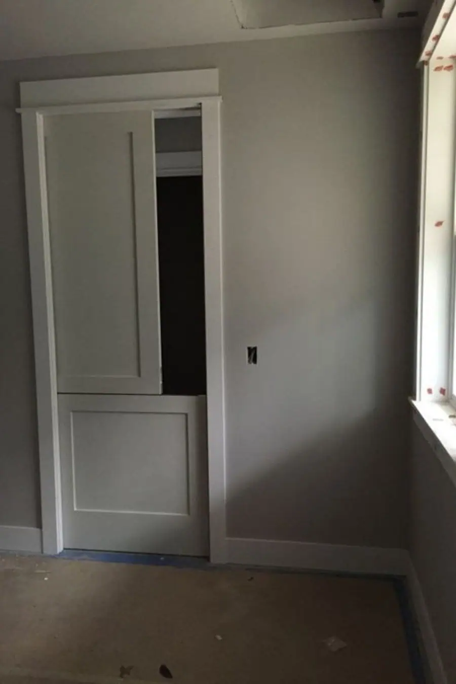 White sliding Dutch door in a minimalistic gray room with natural light from the window.