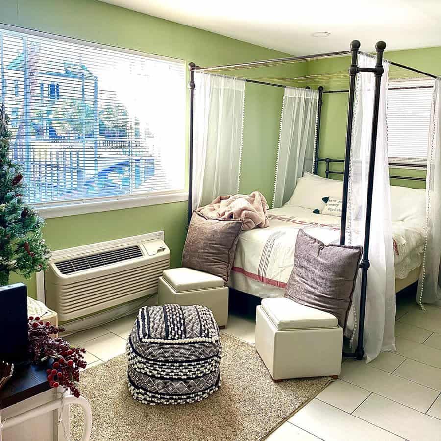 Bright studio with green walls, canopy bed, pouf, and cozy seating near a window.