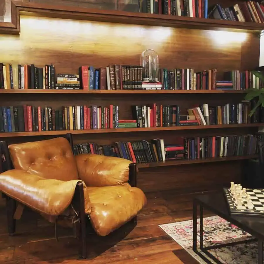 Cozy nook with wooden bookshelves, modern chairs, accent pillows, and ambient lighting.