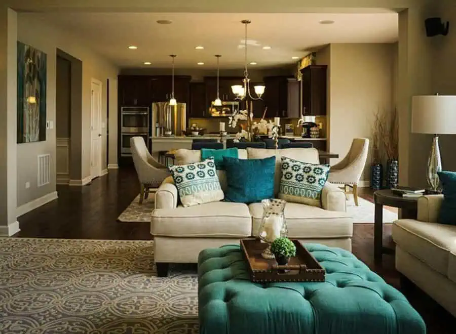 Open-concept living room and kitchen with creamy white furniture, teal accents, and dark wood cabinets.