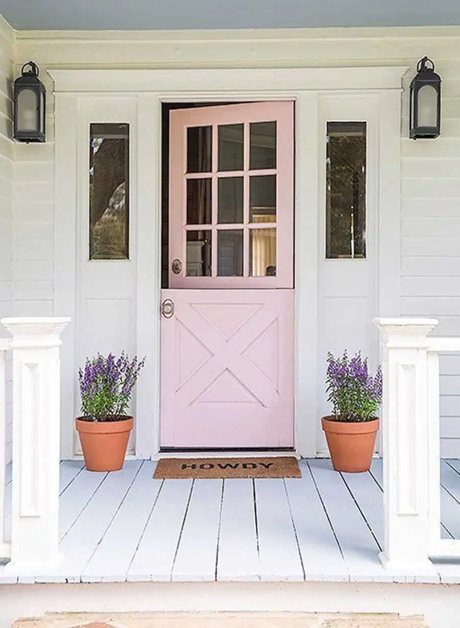 Pink Dutch door with glass panes, white trim, potted flowers, and "Howdy" welcome mat.