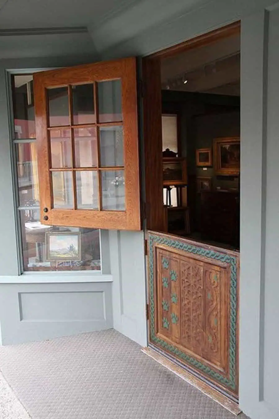 Ornate wooden Dutch door with carved lower panel and glass-paneled top, set in a gray frame.