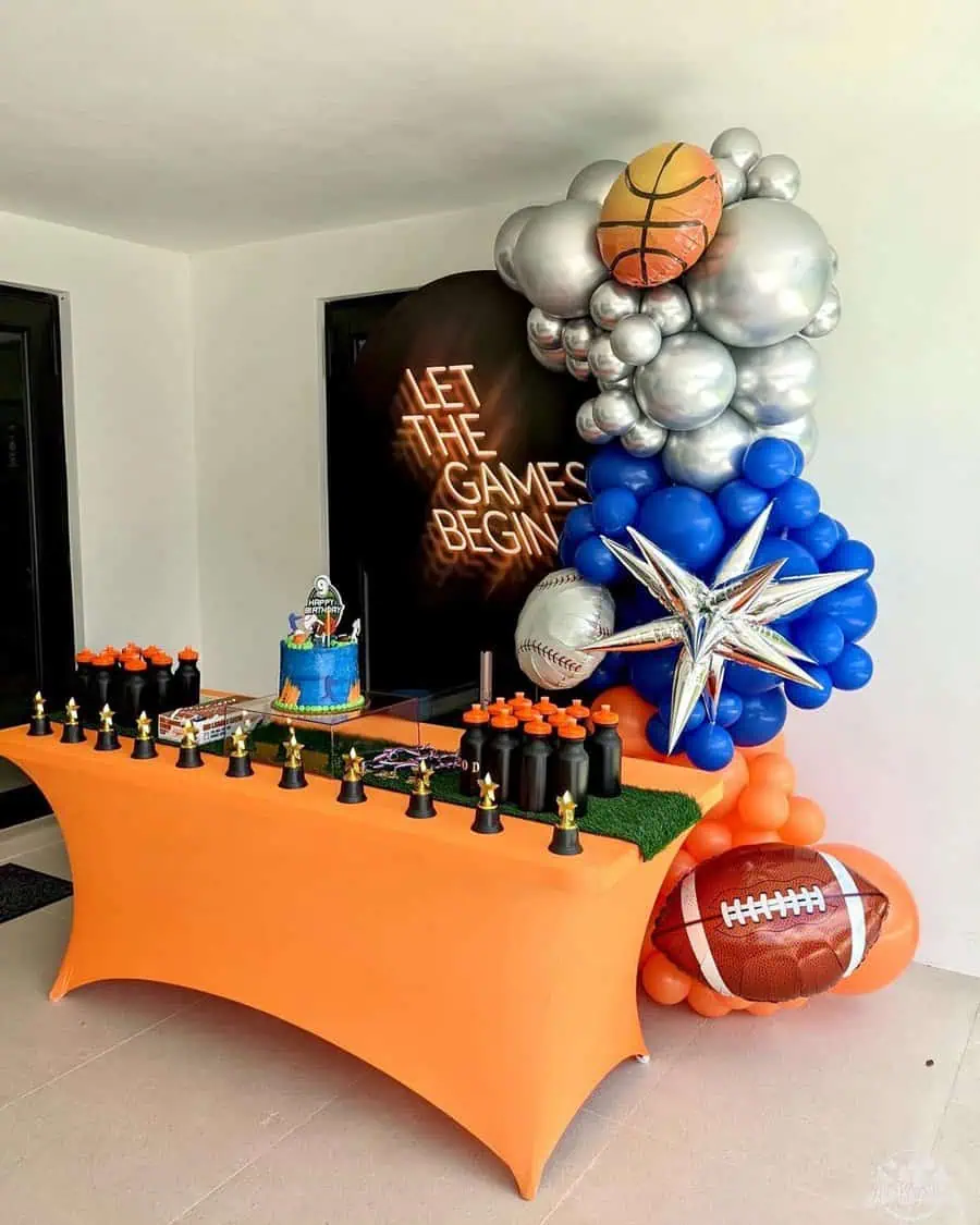 Sports-themed birthday setup with trophy decorations, balloons, and a cake table featuring sports elements.