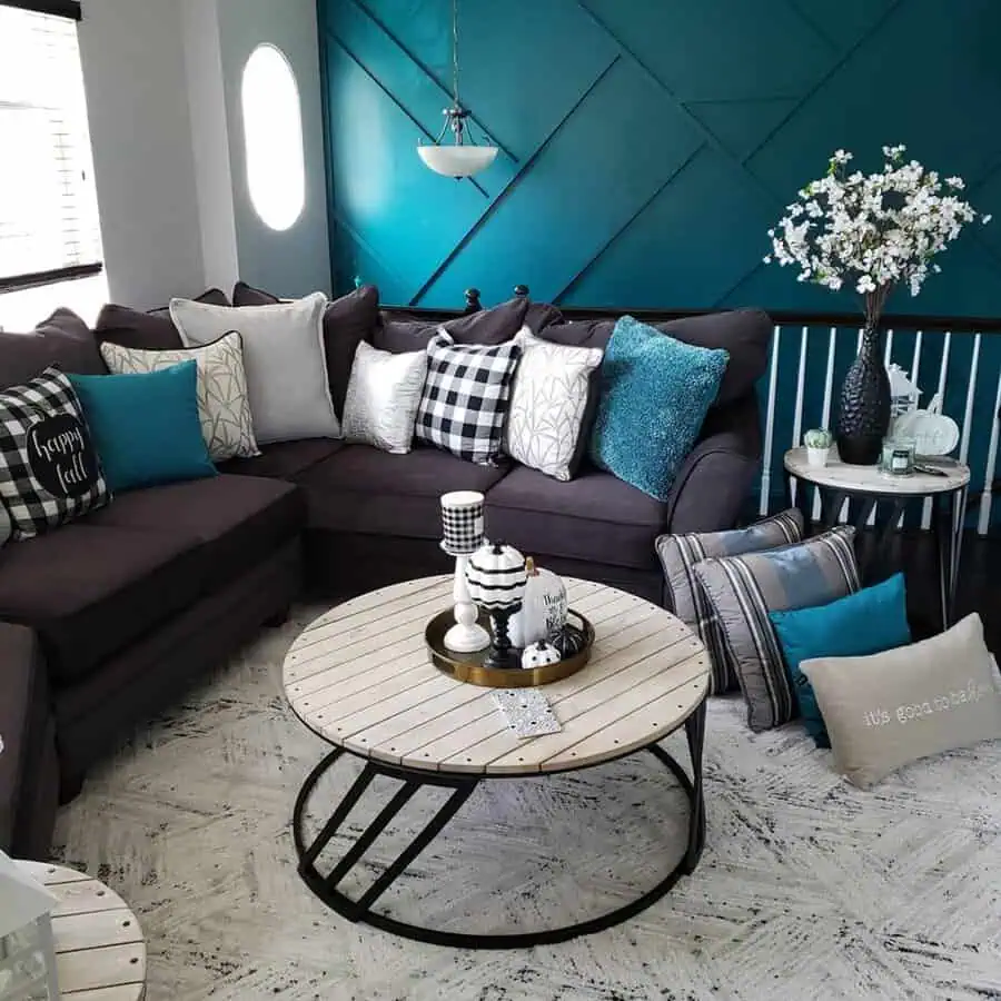 Living room with teal accent wall, dark sectional sofa, patterned pillows, and round coffee table.