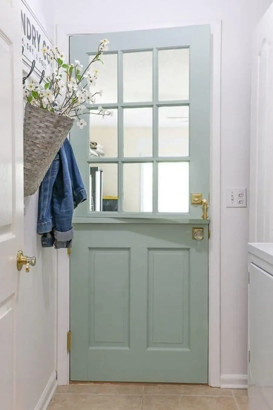 Light green Dutch door with glass panes, brass hardware, and a floral basket in a bright entryway.