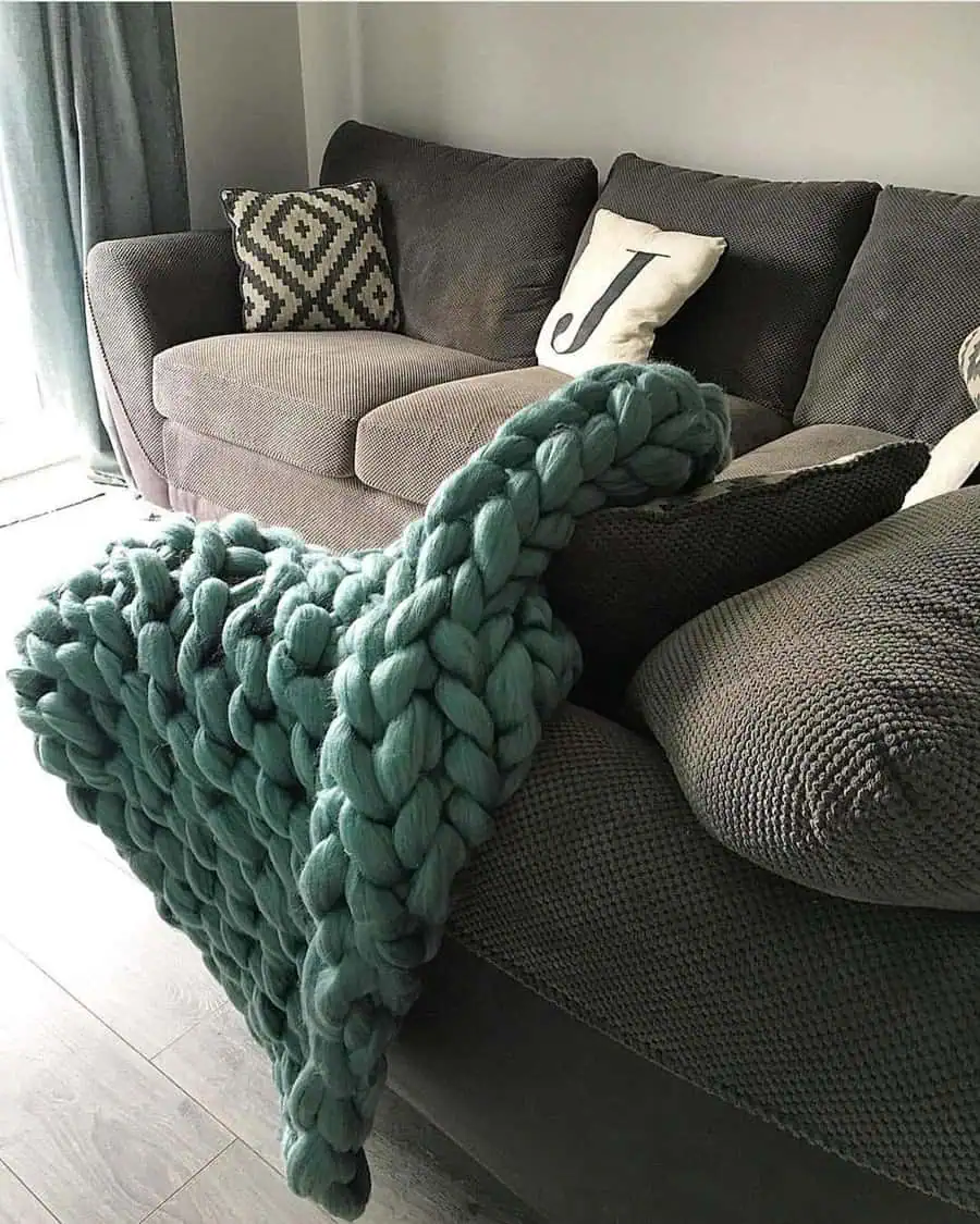 Cozy living room with a chunky teal throw blanket adding texture and warmth to a neutral-toned sofa.