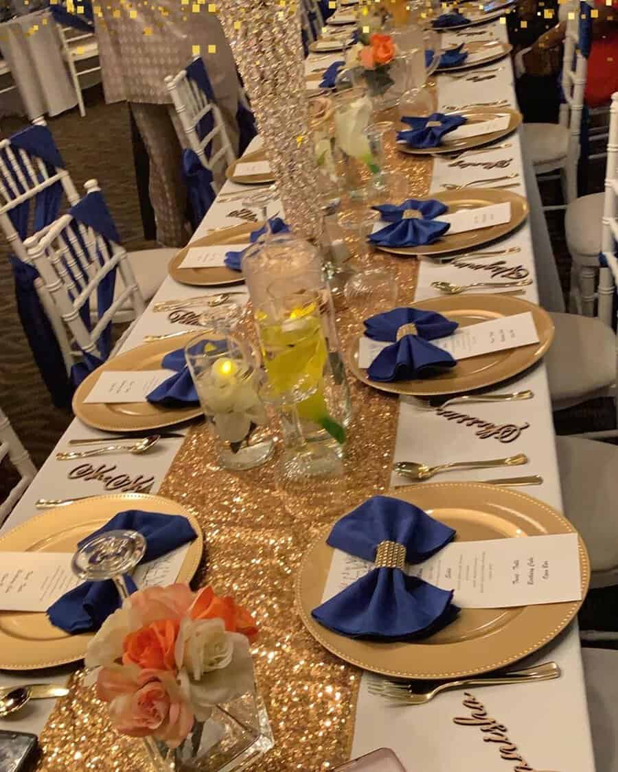 Sparkling gold table runner with navy blue napkins and floral decor for a birthday party.