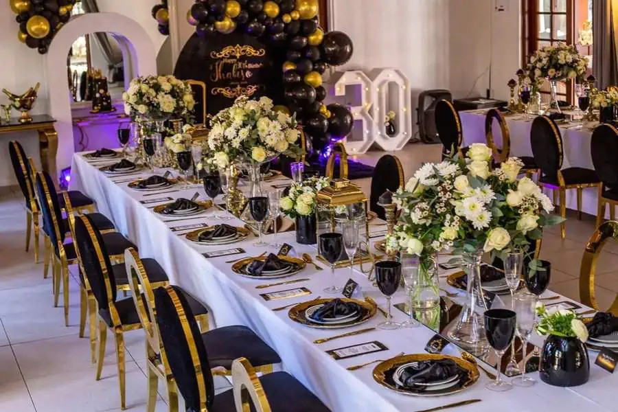 Elegant black and gold table setup with floral centerpieces for a 30th birthday party.