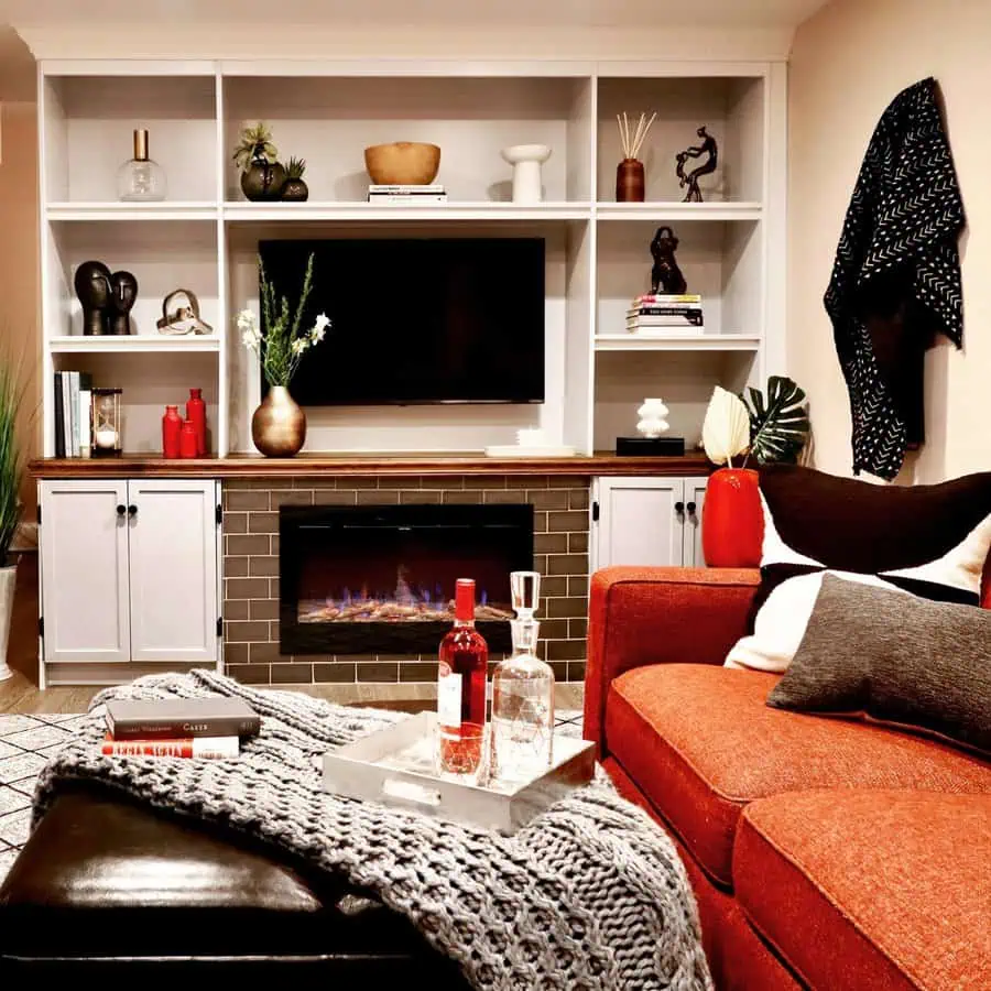 Modern den with built-in shelves, electric fireplace, red sofa, and cozy decorative accents.