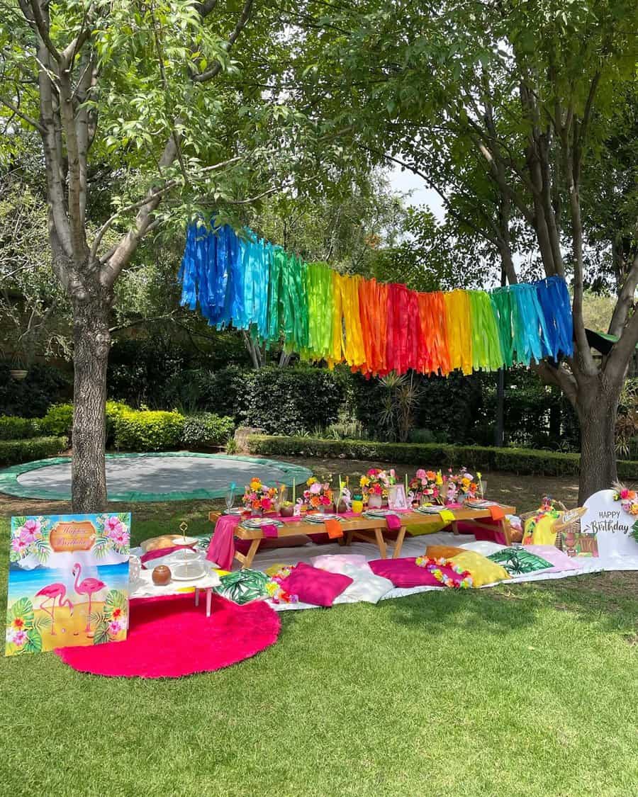 Colorful outdoor birthday setup with rainbow streamers, picnic tables, and vibrant decor.