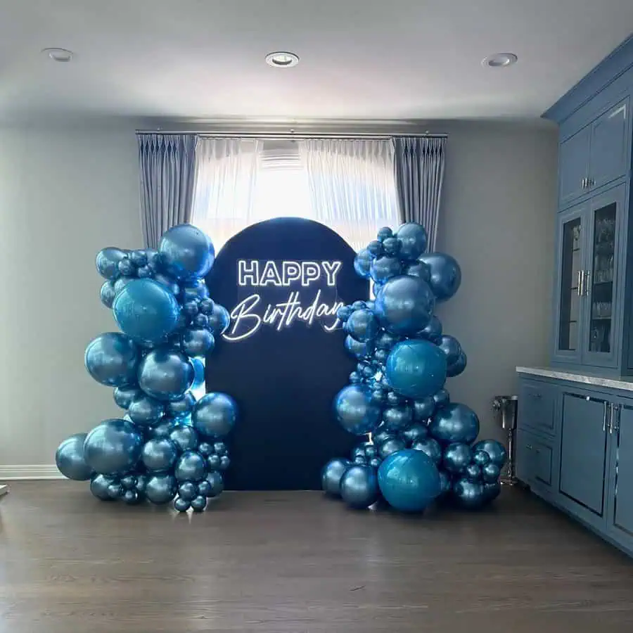 Friend's surprise birthday setup with blue metallic balloons and a neon "Happy Birthday" sign.