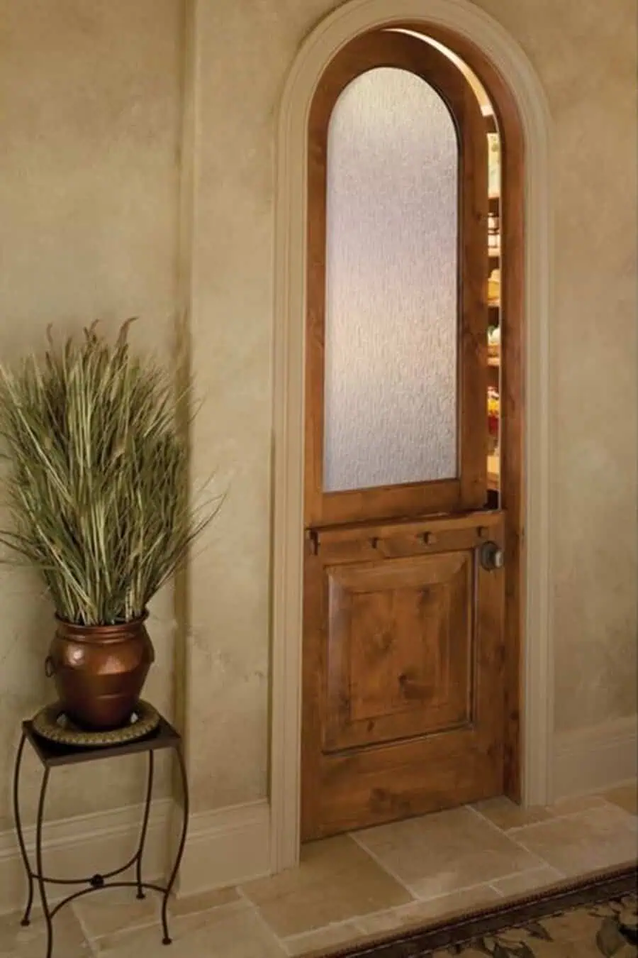 Wooden Dutch door with frosted glass panel, arched frame, and potted plant in a cozy interior.