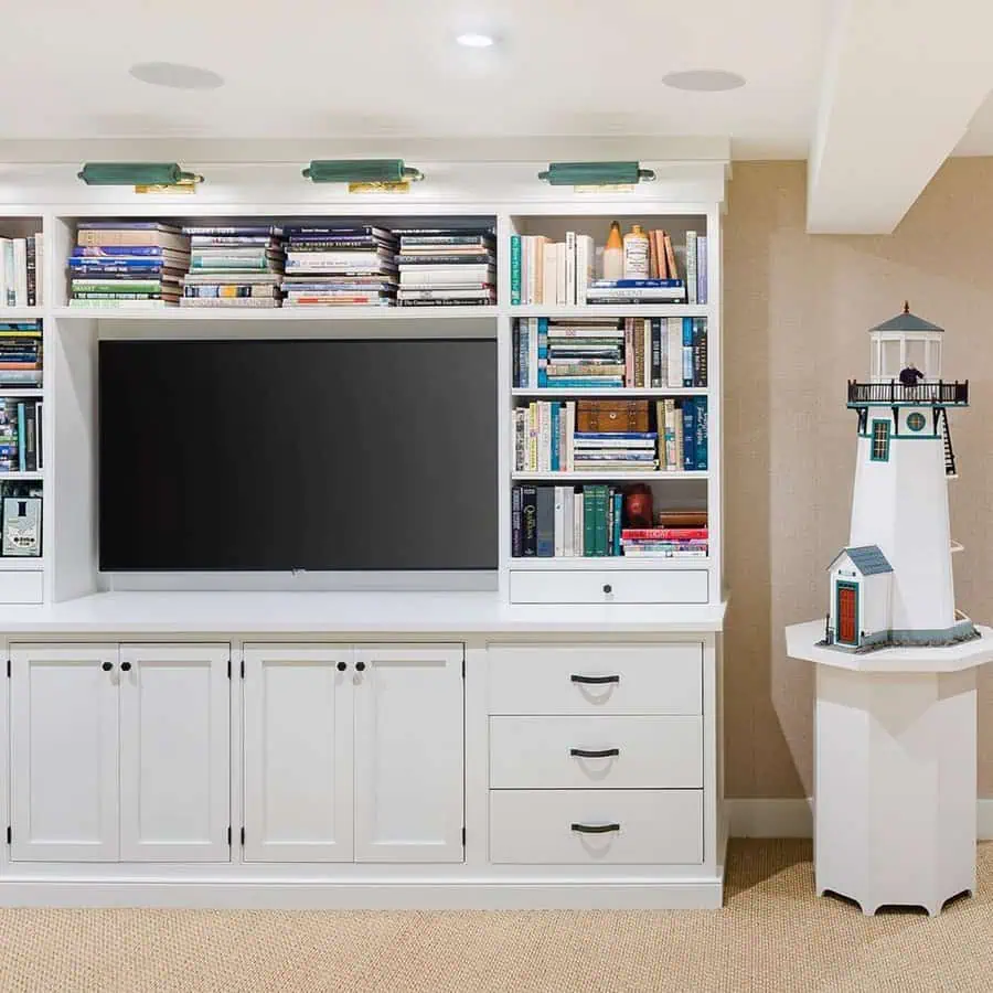 White built-in media center with bookshelves, TV, and a lighthouse model on a side table.