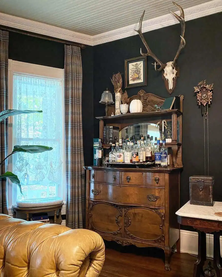 Vintage bar cabinet with antler decor, dark walls, plaid curtains, and a cozy leather sofa.