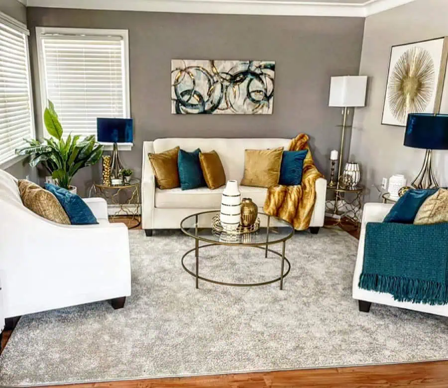 Luxurious living room with white sofas, teal and gold accents, and chic gold tables.