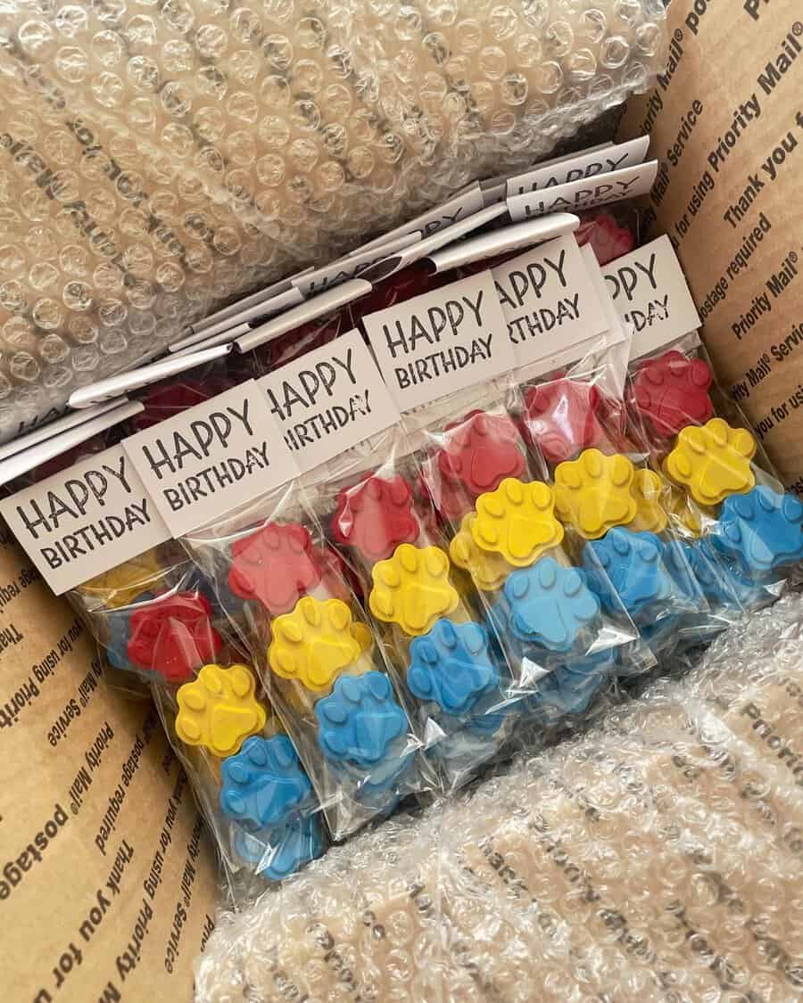 Packaged paw-shaped birthday party favors with "Happy Birthday" tags in a box.