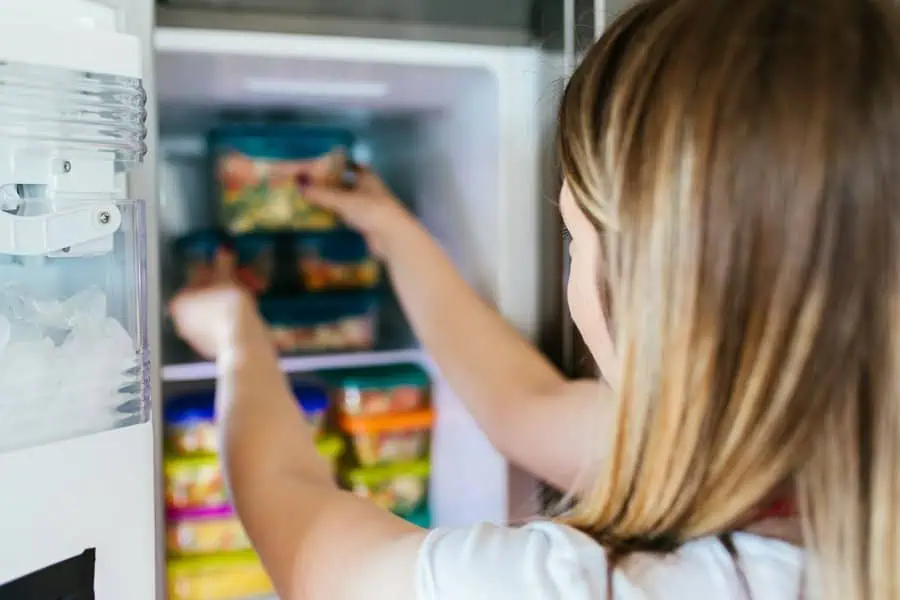 Woman placing food containers into an organized refrigerator drawer.