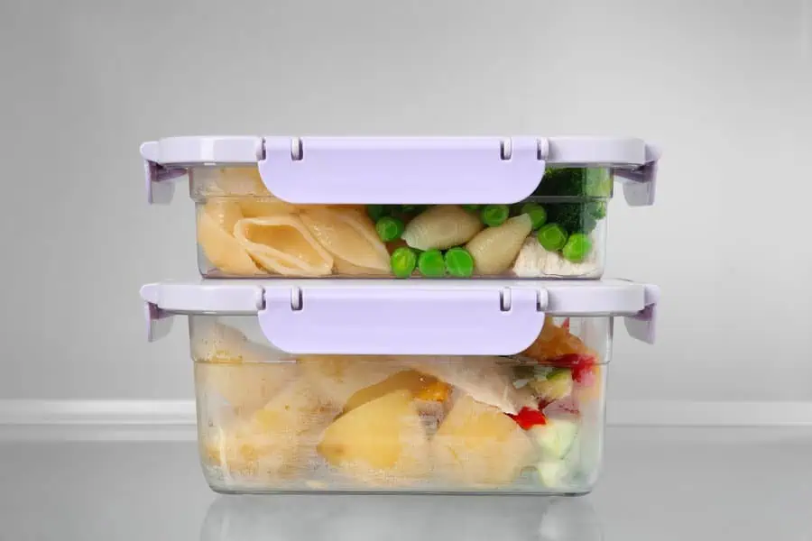 Stacked food containers with pasta, peas, and vegetables stored in a refrigerator.