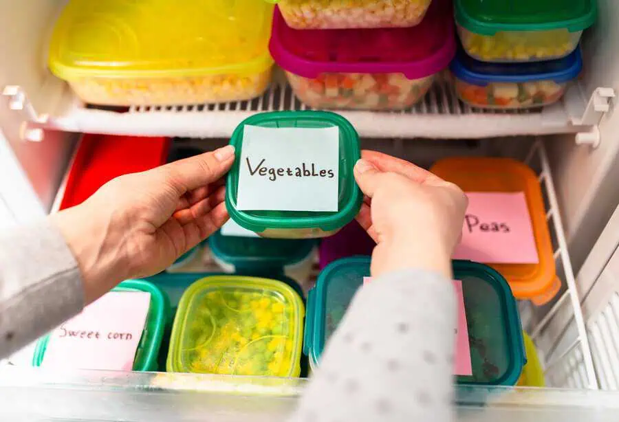 Labeled food containers with vegetables and peas neatly organized in a freezer.