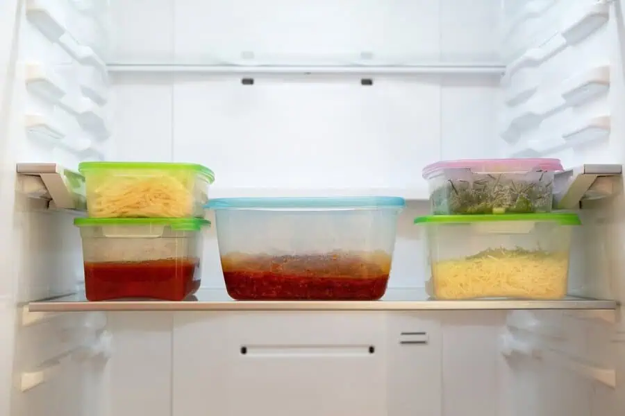 Stacked containers with pasta, sauce, and greens neatly stored in a refrigerator.