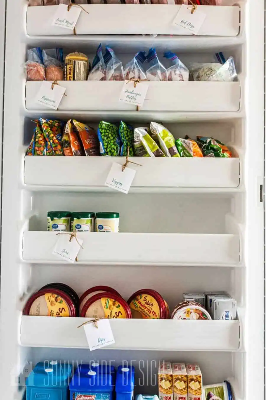 Labeled freezer door shelves with neatly organized meats, veggies, juices, and dips.