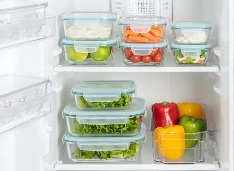 Glass containers with fresh vegetables, fruits, and peppers organized in a refrigerator.