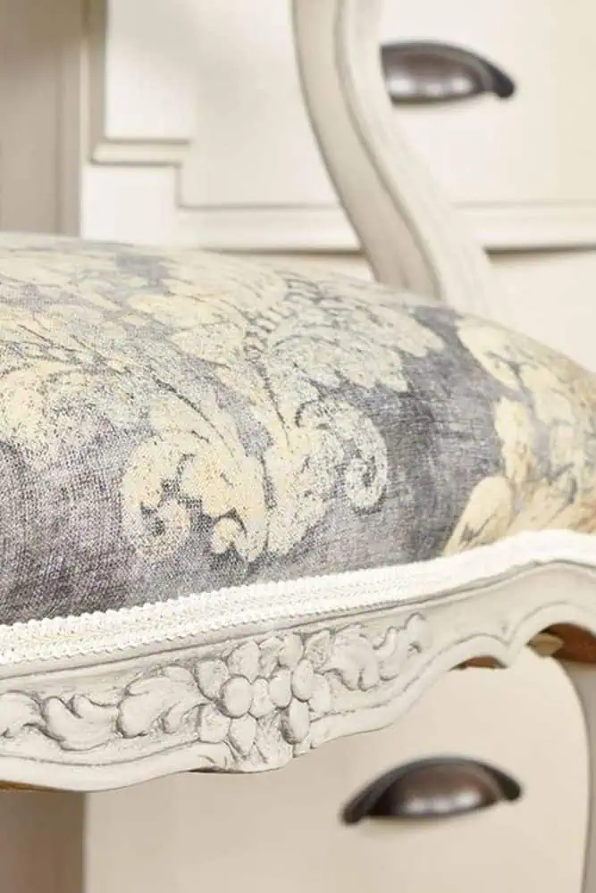 Close-up of a vintage chair with floral upholstery and carved wooden details.