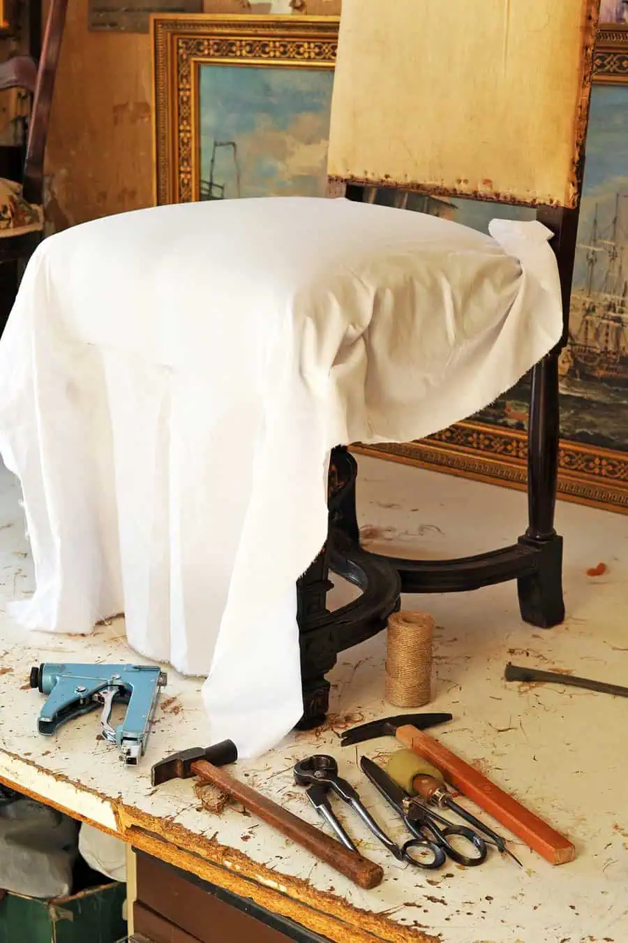 Chair with white fabric ready for reupholstery, surrounded by tools like a staple gun and hammer.