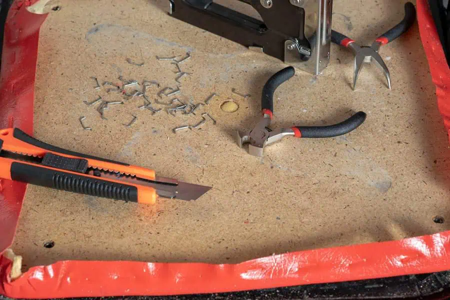 Staple remover, cutter, pliers, and staples on a wooden board for upholstery work.