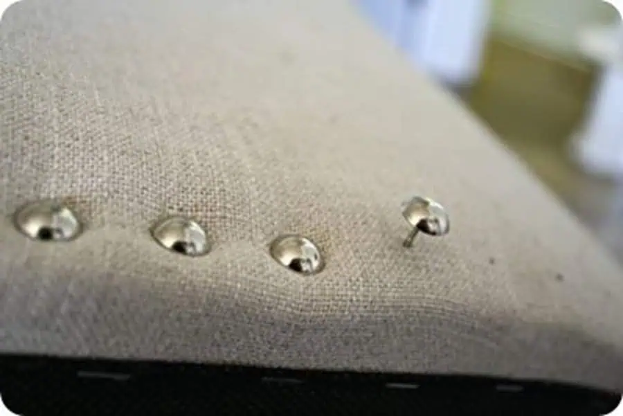 Close-up of silver decorative tacks being added to linen upholstery.