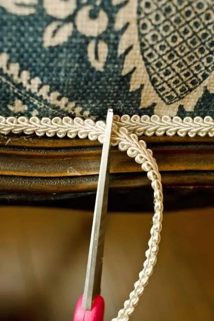 Close-up of scissors trimming decorative cord on upholstered furniture edge.