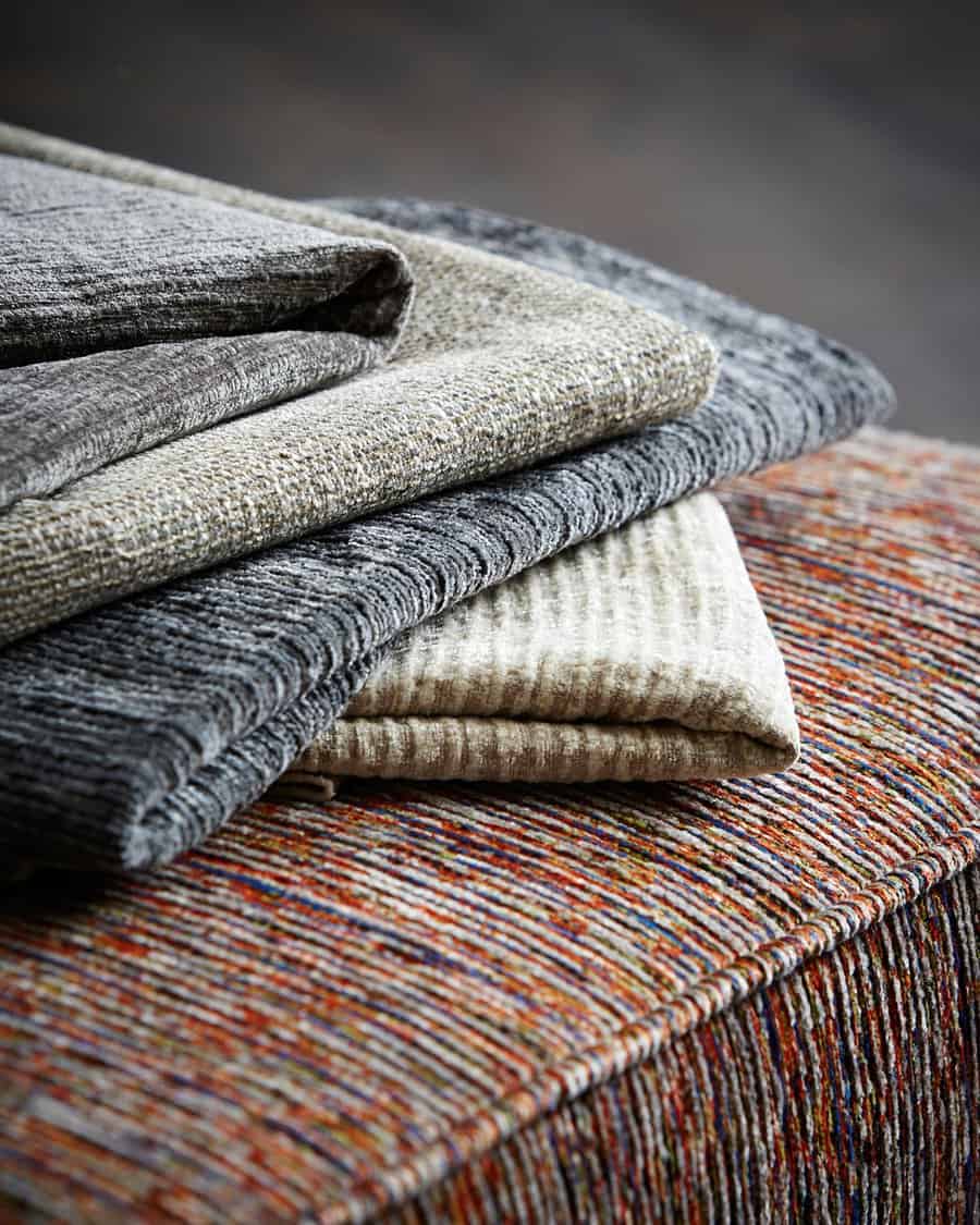 Stack of textured fabric in neutral and colorful tones for upholstery or furniture projects.