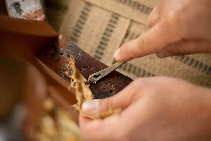 Hands removing old fabric and tacks from a wooden chair frame during reupholstering.