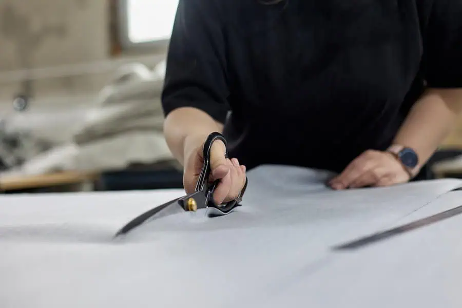 Person cutting fabric with large scissors on a work table for upholstery purposes.