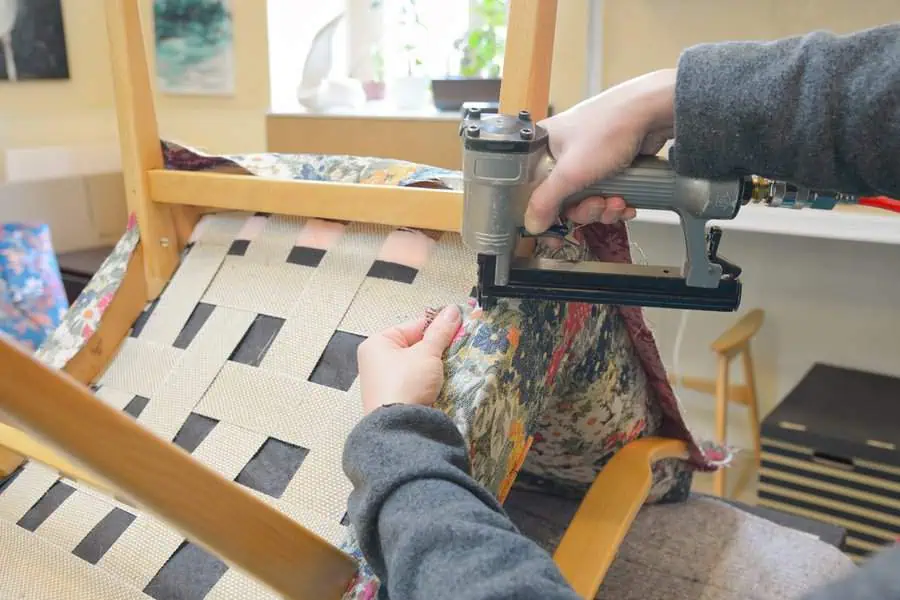 Person using a staple gun to secure fabric on a chair frame during reupholstery work.